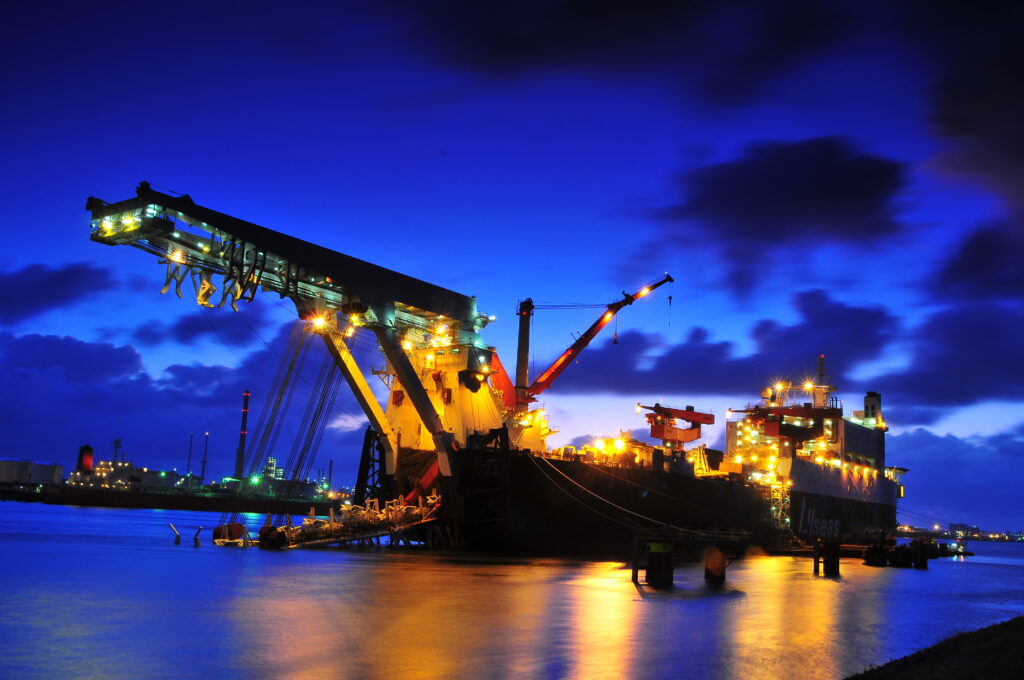 Haven van Rotterdam in de avond met een kraan en een schip die verlicht zijn.
